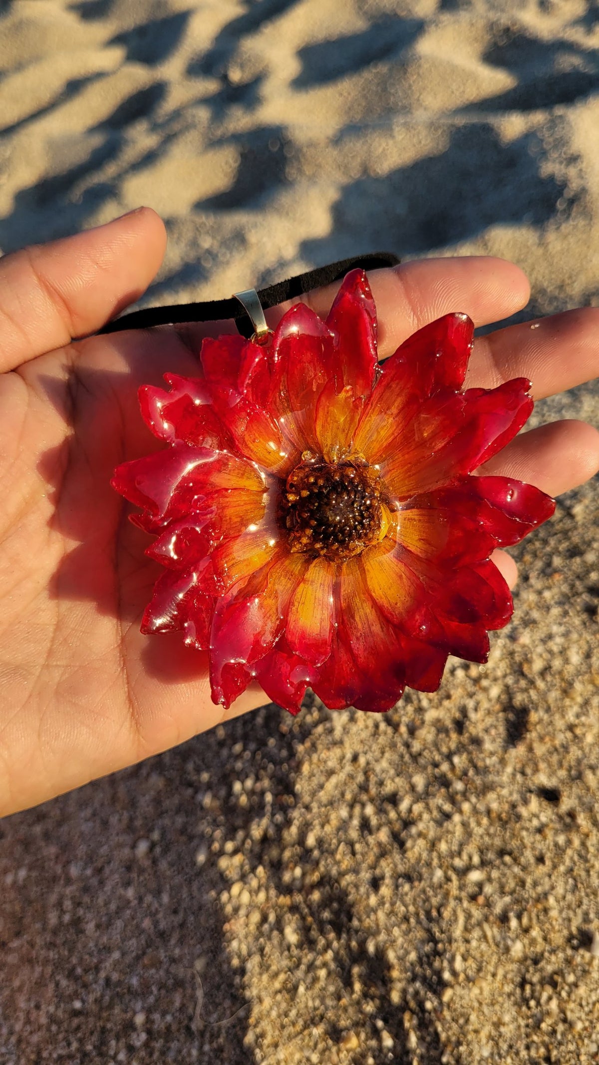 A preserved strawflower pendant held in an open palm on the sand