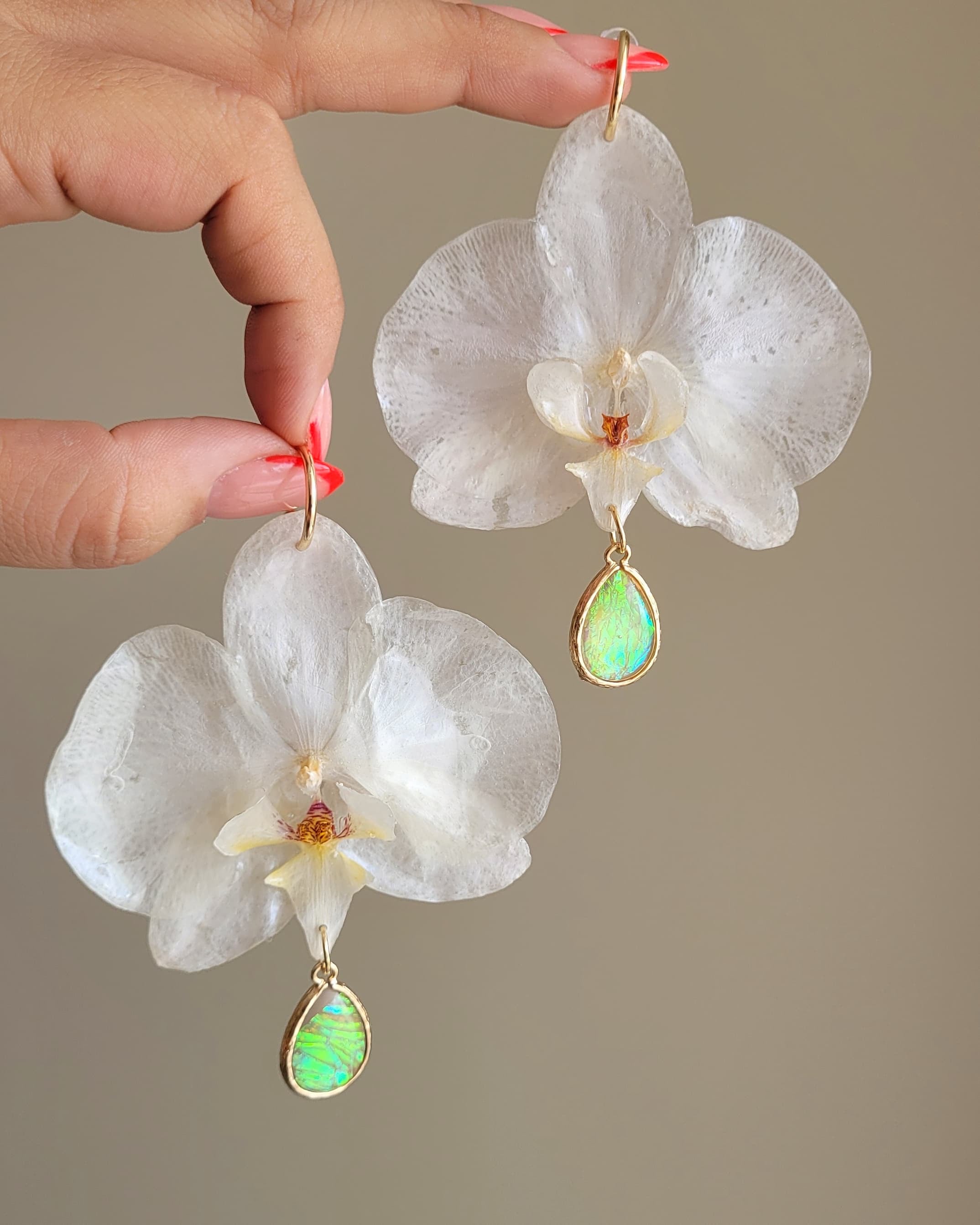 White Phalaenopsis orchid earrings in resin with opal drops on gold-filled hooks, held in hand