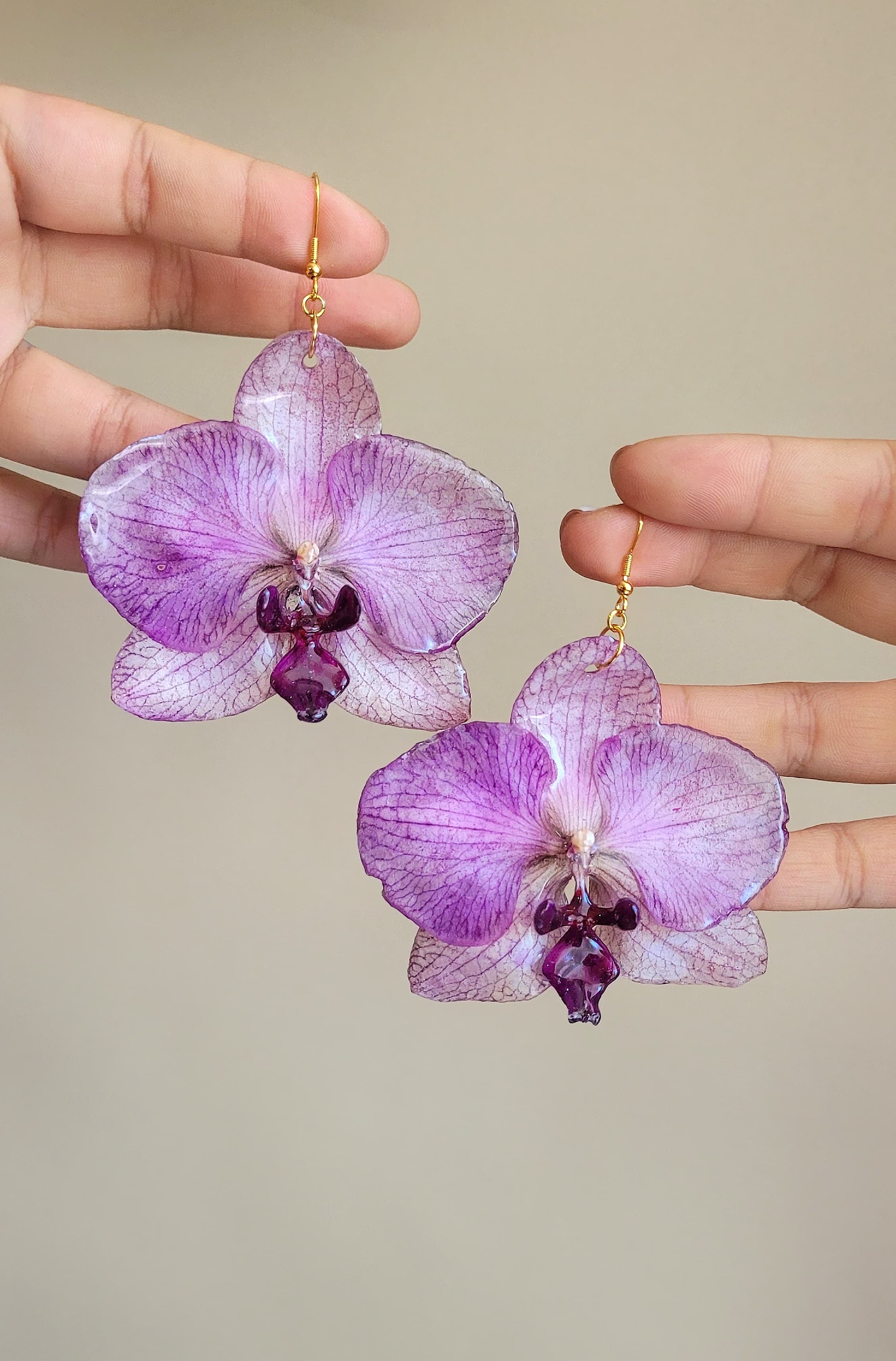 Purple Phalaenopsis orchid earrings in resin with gold-filled hooks, held in hand