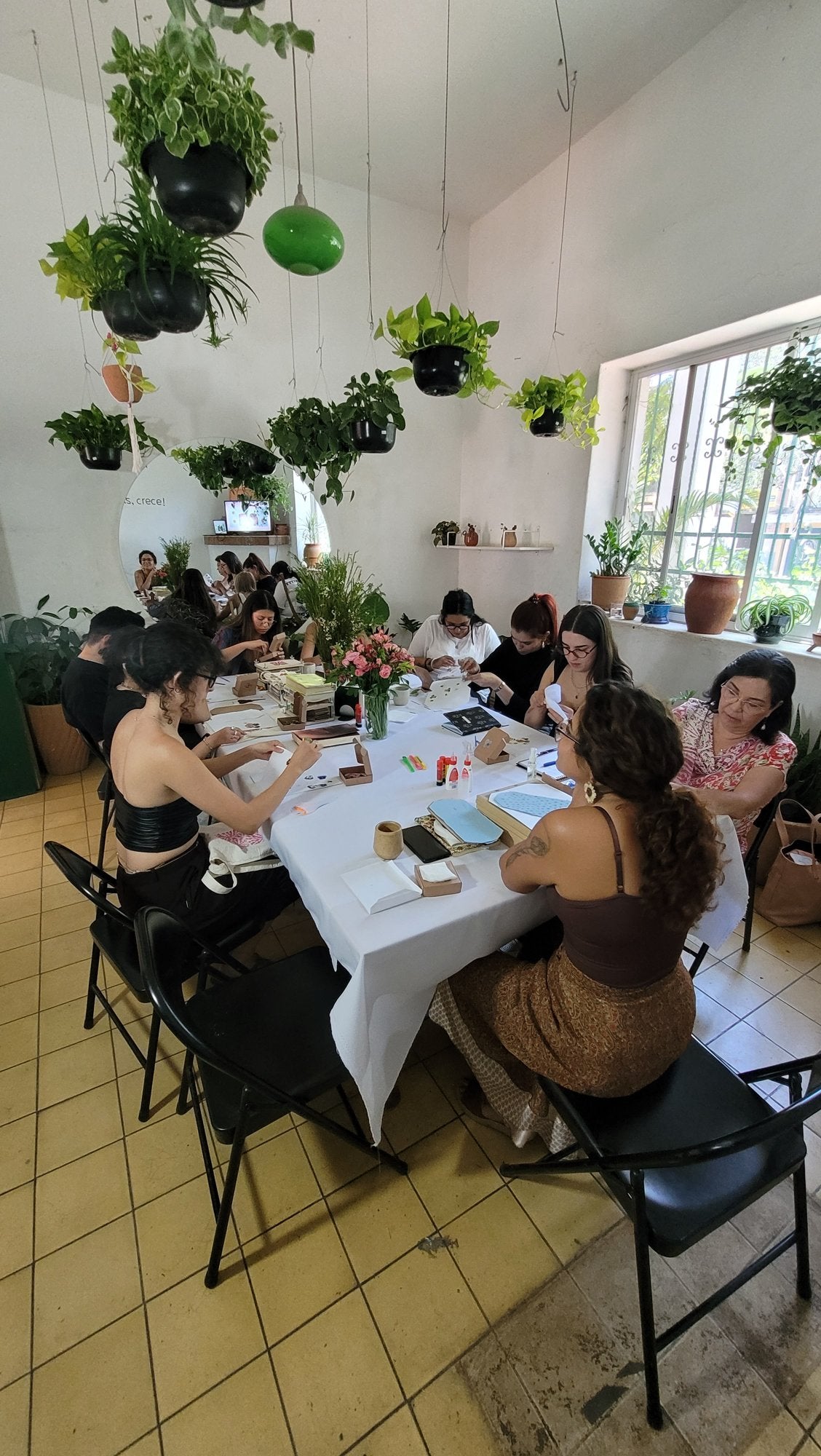 A private botanical-jewelry workshop group working at a table in a bright, plant-filled room.