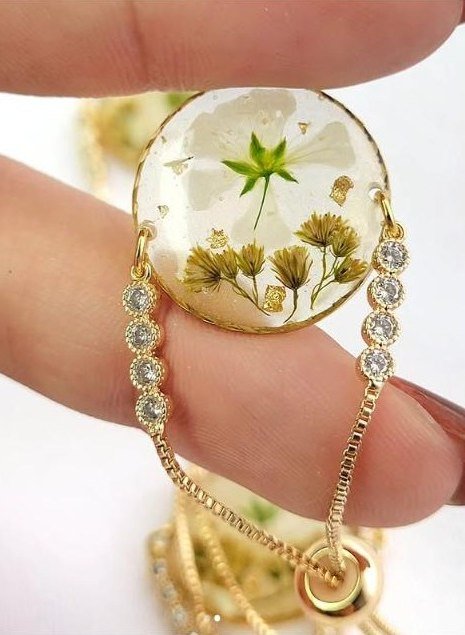 Close-up of one bracelet: a white flower and gold flakes in clear resin
