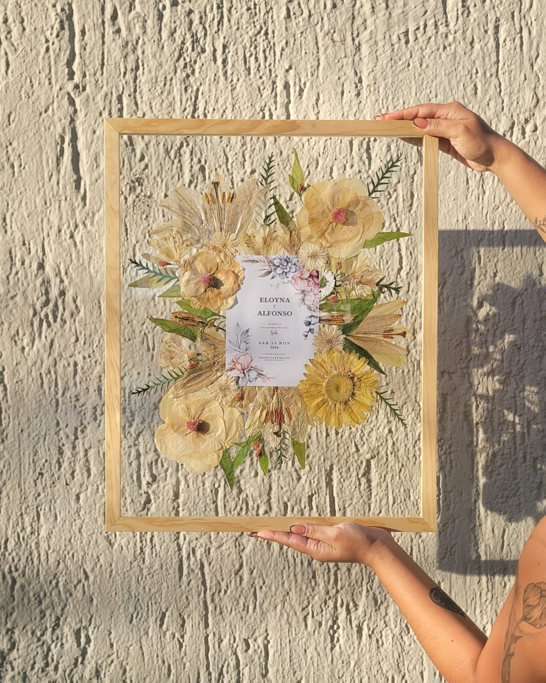 Eloyna and Alfonso's pressed wedding flowers in a pine frame, held up in golden-hour light