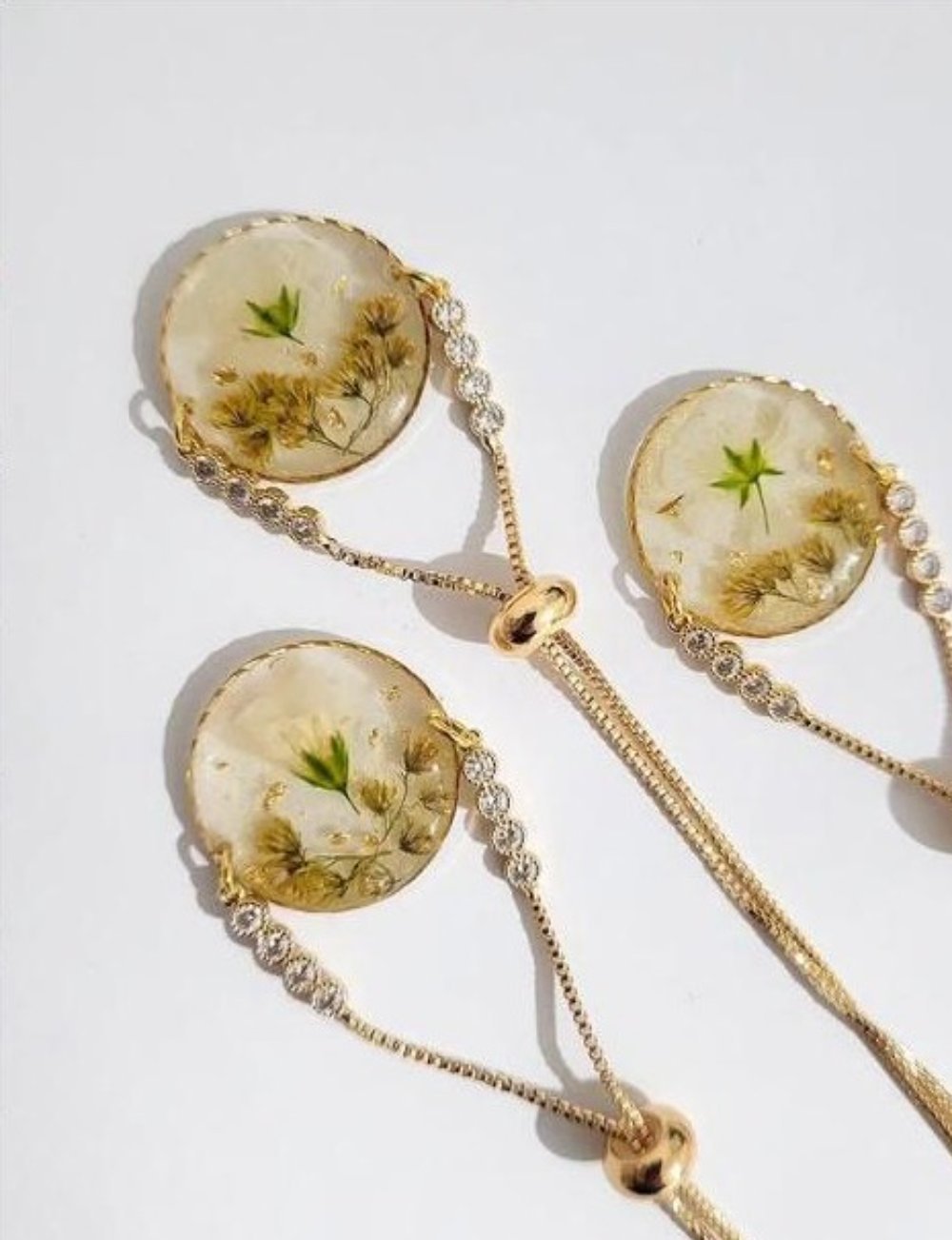 Three matching resin bracelets from a Cancún bouquet, gold chains with preserved white blooms